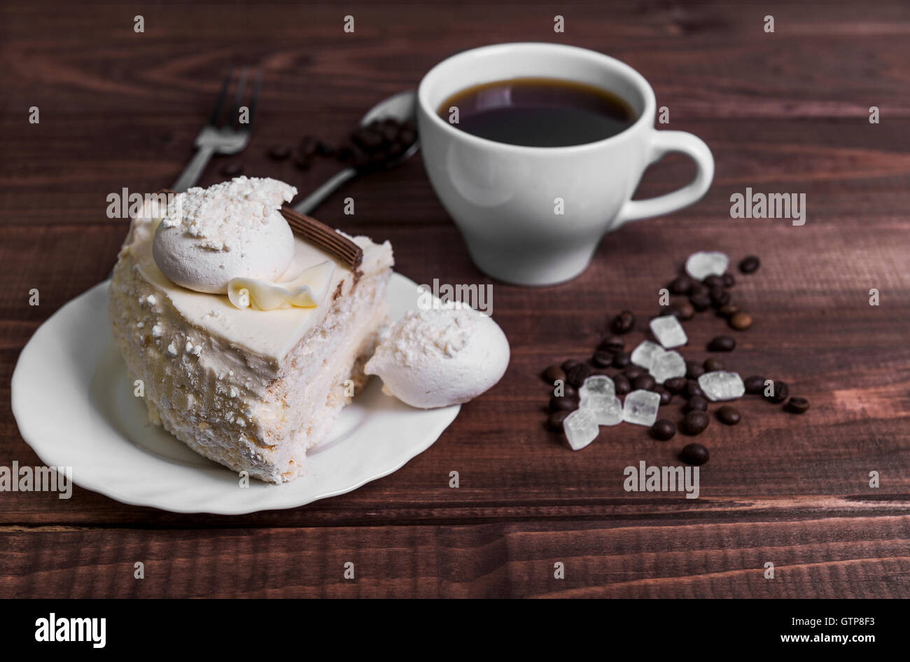 Su un tavolo di legno delicatezza - un piattino con un pezzo di torta e una tazza di meringa con i chicchi di caffè e zucchero, Forchetta, Cucchiaio Foto Stock