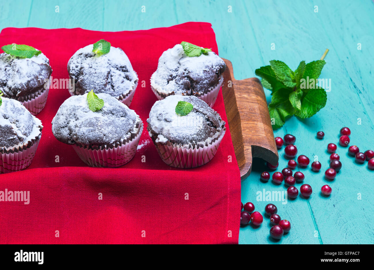 Sulla luce di un tavolo in legno in stile rustico, qualche muffin al cioccolato in carta spolverati con zucchero a velo sulla parte superiore e menta fresca lea Foto Stock