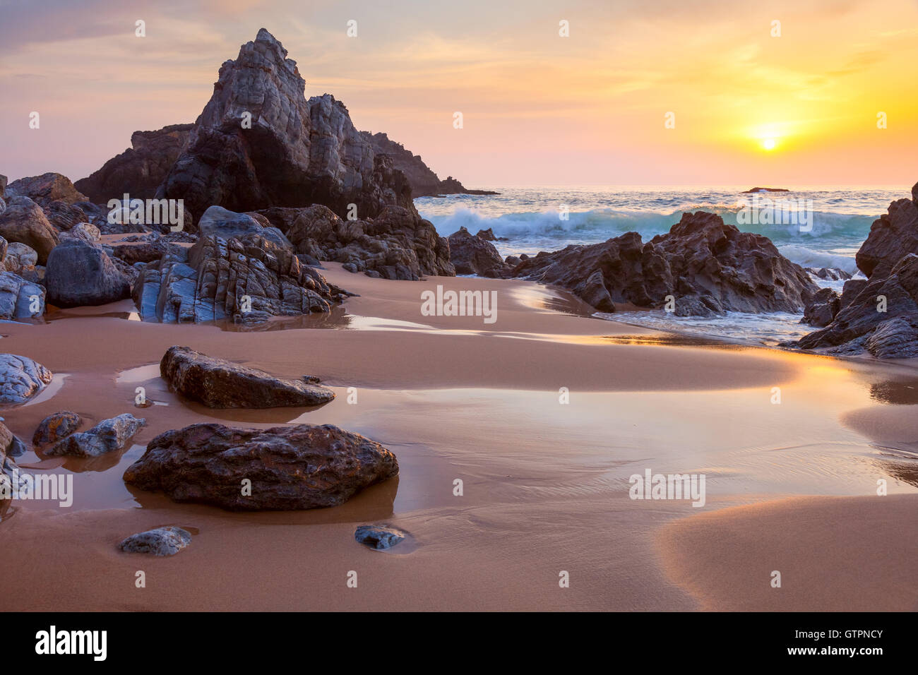 Fantastico grandi rocce e sassi sulla spiaggia dell'oceano al tramonto dorato paesaggio Foto Stock