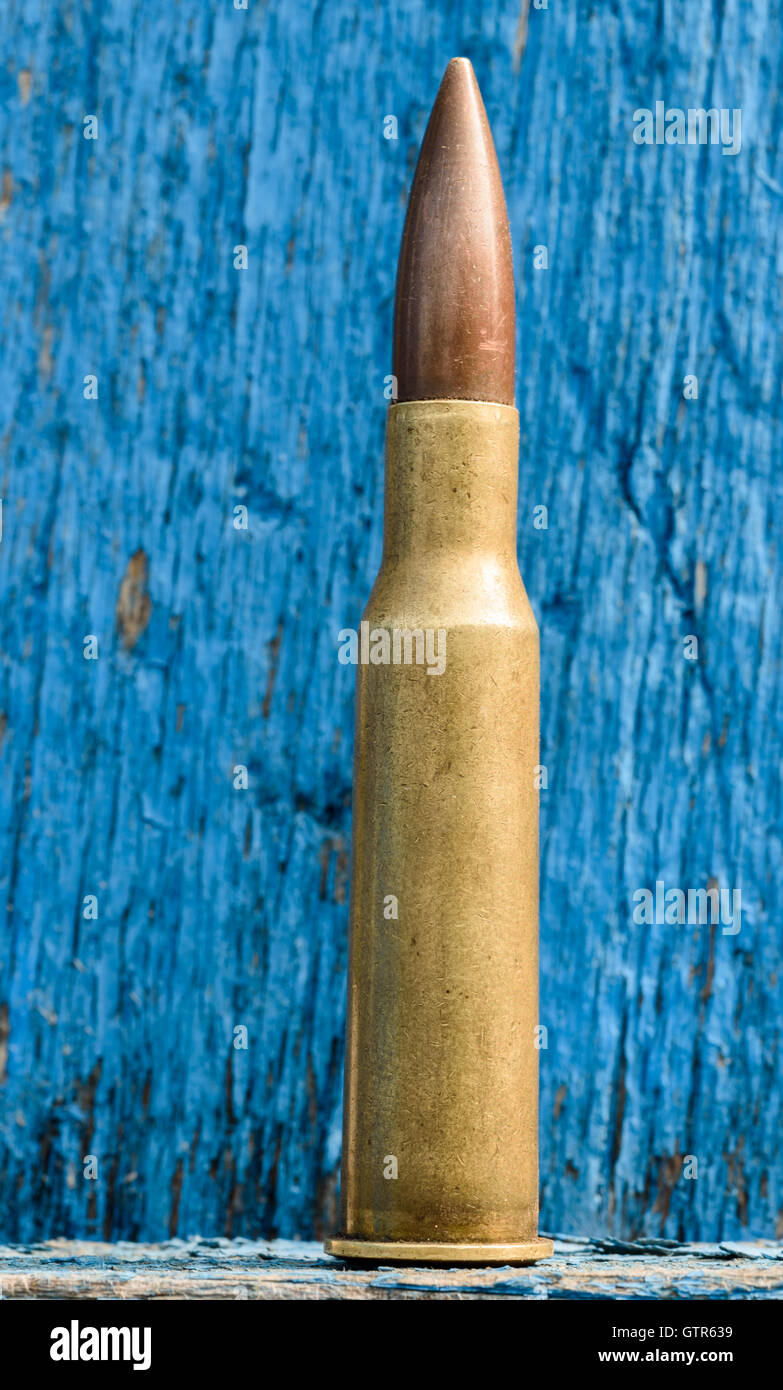 7,62 mm guscio di munizioni tipicamente usato per il Kalashnikov fucile da assalto montante eretta contro una copia dello spazio in legno di colore blu Foto Stock
