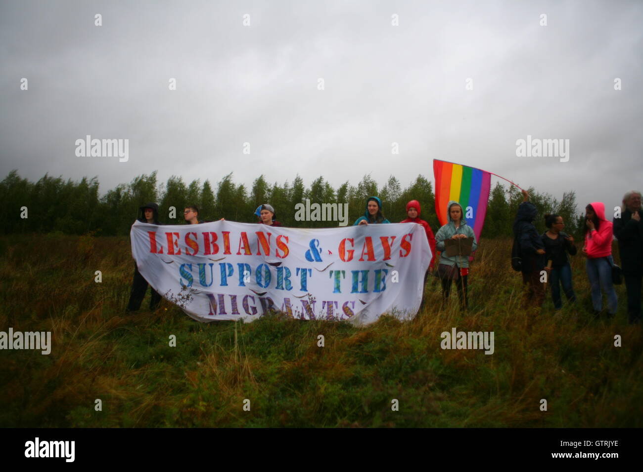 Milton Ernest, Bedford, Regno Unito. 10 settembre 2016. Un gruppo di manifestanti si trova in un campo erboso con uno striscione che recita "Lesbians & Gays Support the Migrants" accanto a una bandiera arcobaleno. La protesta evidenzia il sostegno intersettoriale tra le comunità LGBTQ+ e i diritti dei migranti. Centinaia di manifestanti protestano contro il recinto del centro di detenzione Yarls Wood chiedendo la chiusura della struttura. Penelope Barritt/Alamy Live News Foto Stock