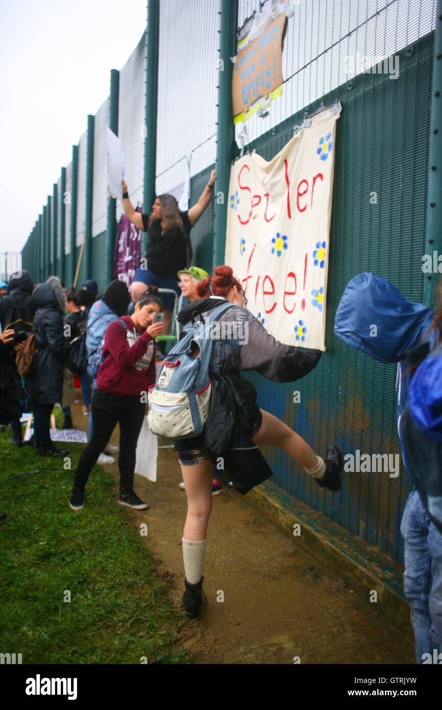 Milton Ernest, Bedford, Regno Unito. 10 settembre 2016. Un gruppo di manifestanti si riunisce vicino a un'alta recinzione metallica, attaccando striscioni e cartelli in una protesta pacifica. Uno striscione prominente recita "sei der Friede!" (“sii la pace!”), adornata di motivi floreali. La scena suggerisce l'attivismo di base in condizioni climatiche umide. Centinaia di manifestanti protestano contro il recinto del centro di detenzione Yarls Wood chiedendo la chiusura della struttura. Penelope Barritt/Alamy Live News Foto Stock