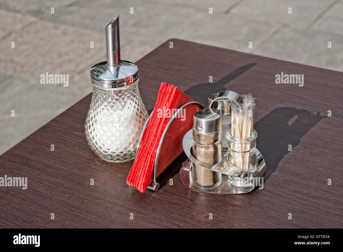 Sale e pepe, Sugar Bowl, rosso di tovaglioli di carta su un tavolo marrone di un piccolo street cafe. Nessuno attorno a. Benvenuti all'estate cafe Foto Stock