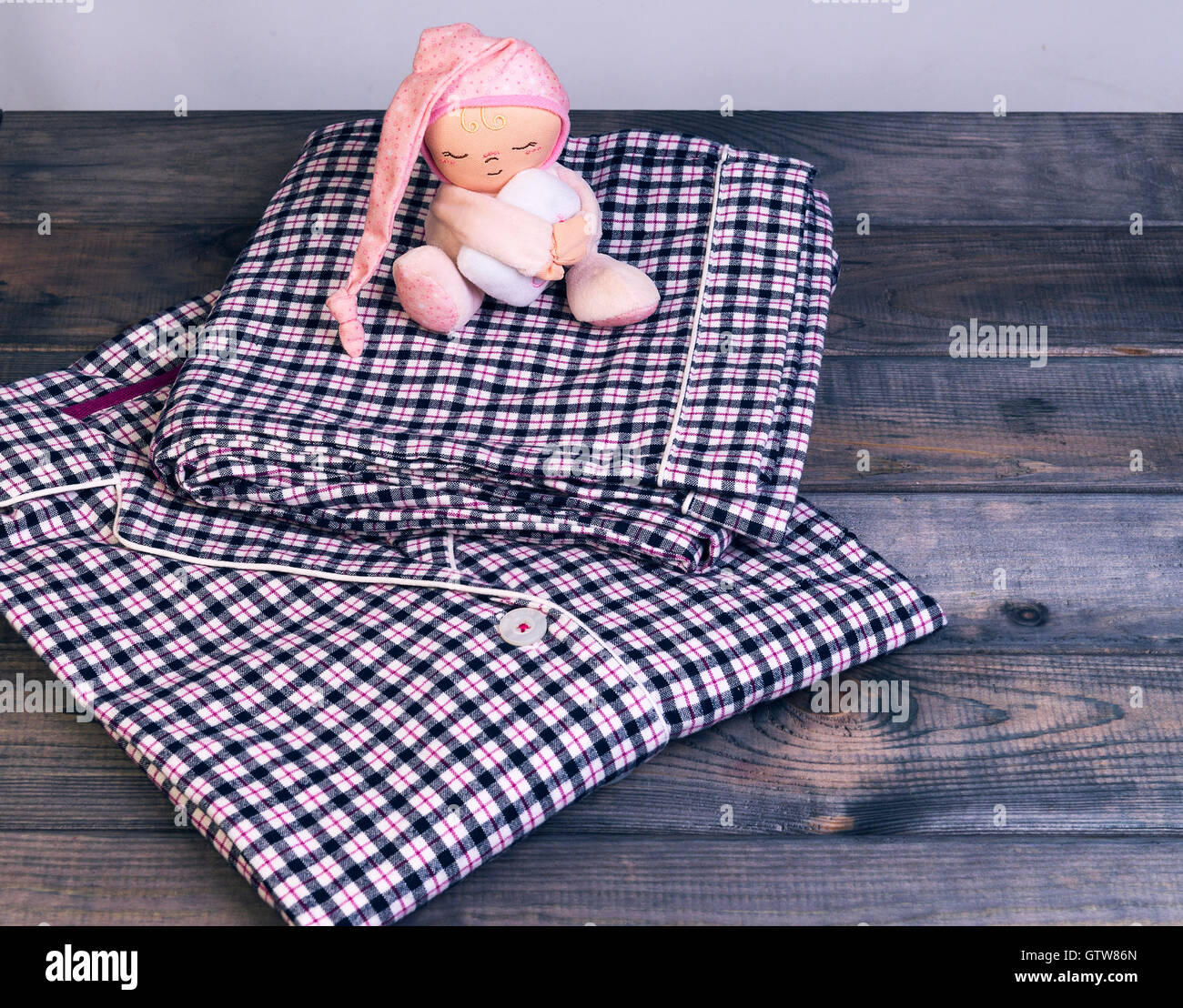 Su un tavolo di legno a scacchi pigiami di flanella e un soffice bambola giocattolo dormire uomo in un cappello rosa con un cuscino sotto le sue mani Foto Stock