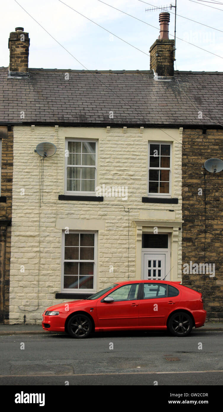 Un rosso brillante auto è parcheggiata fuori una crema colorata terrazza casa in Skipton North Yorkshire. Foto Stock