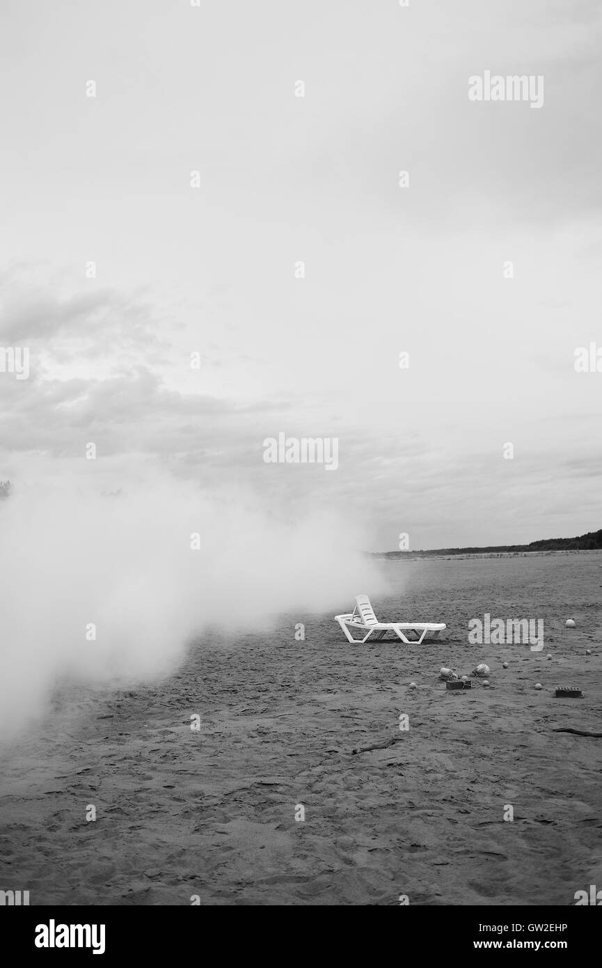 Svuotare chaise-longue sulla spiaggia vuota che sopraggiungono con la nuvola di fumo bianco. Foto Stock