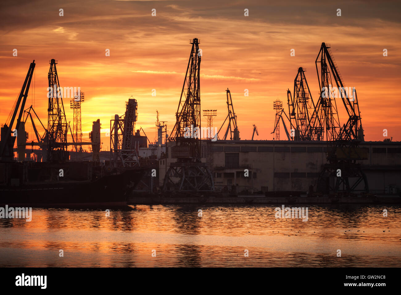 Sagome di gru industriali e le navi da carico nel porto di Varna al tramonto Foto Stock