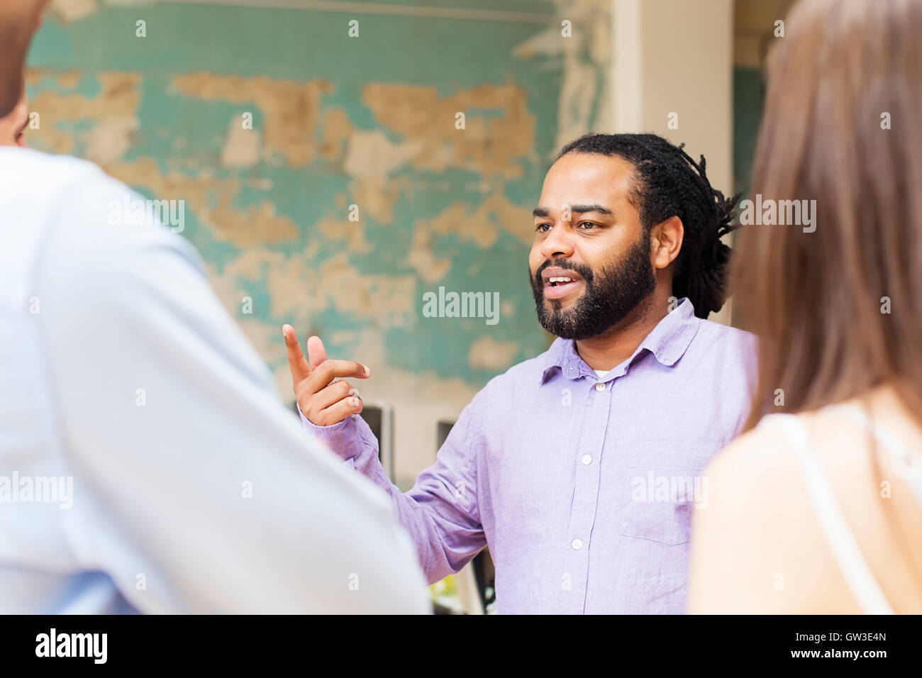 Giovane americano africano uomo che parla di qualcosa di altri giovani in ufficio Foto Stock