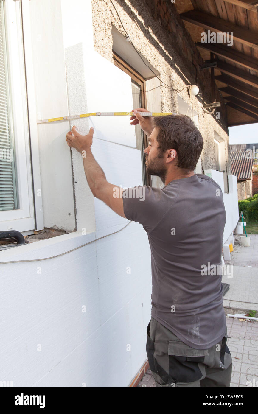 Uomo che lavora con il misuratore di isolamento termico della facciata. Foto Stock