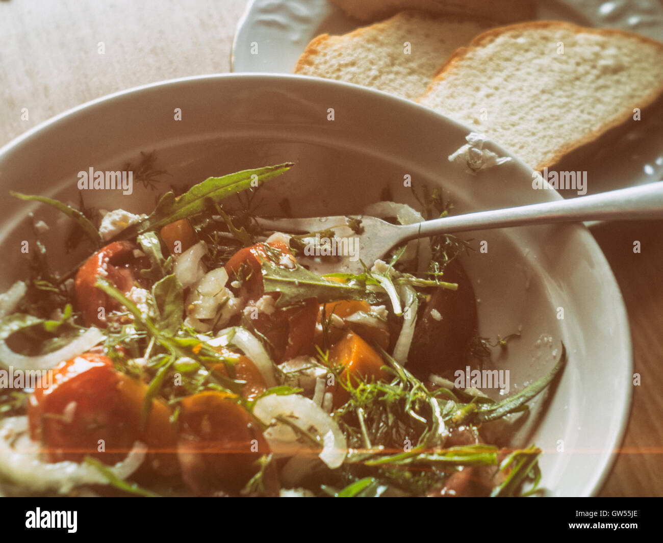 Insalata fresca con nero, rosso e giallo i pomodori, la cipolla, verde spezie e formaggio feta formaggi una spruzzata di olio extra vergine di oliva. Vecchia macchina fotografica Foto Stock