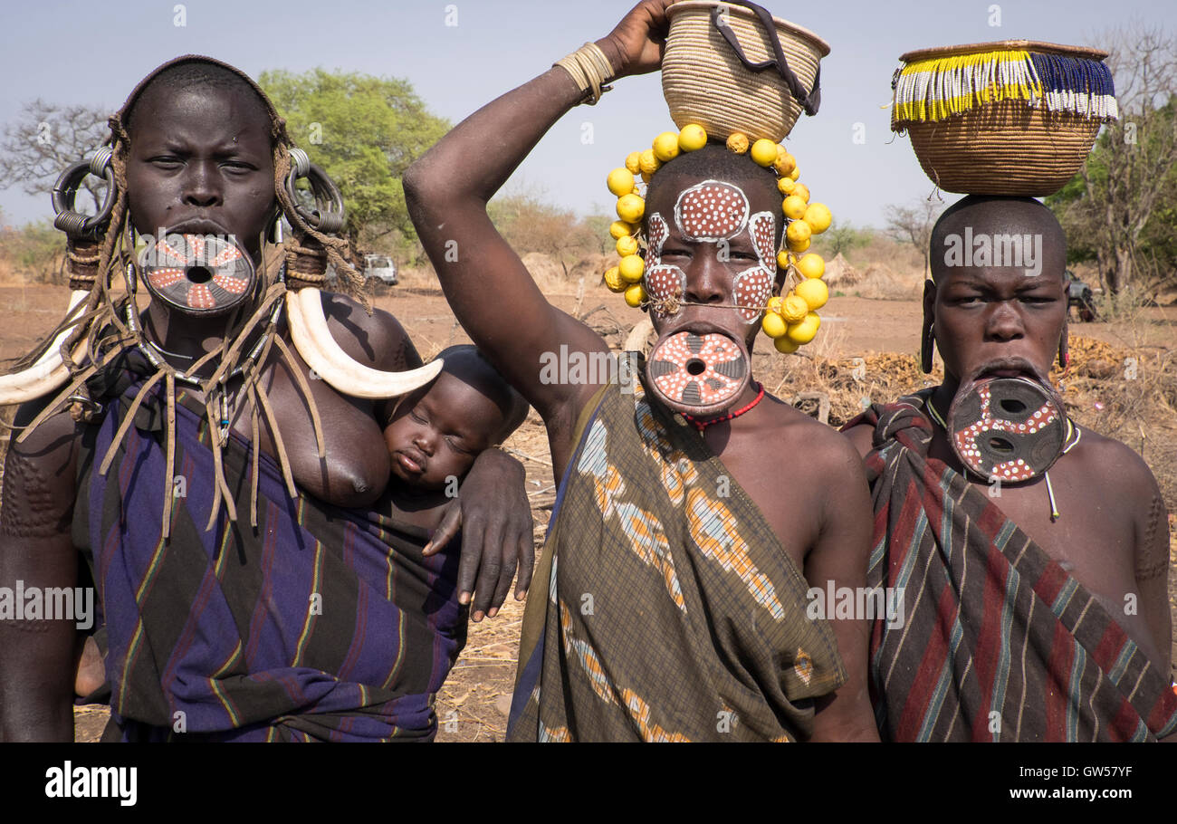 Tre donne Mursi della valle dell'Omo in Etiopia con labbro di piastre ossee, orecchini, copricapo e corpo rituale vernice, uno con il bambino Foto Stock