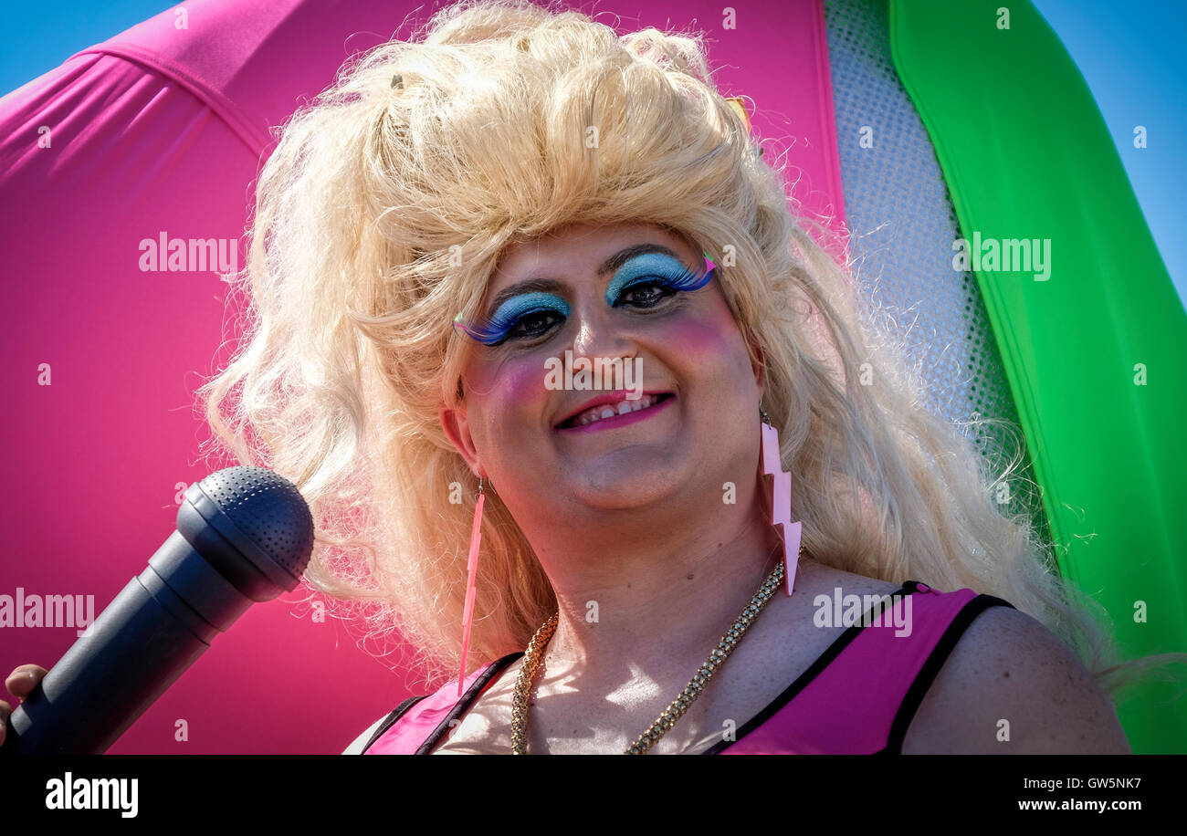 Drag queen in costume e parrucca vestito per una sfilata di carnevale con microfono Foto Stock