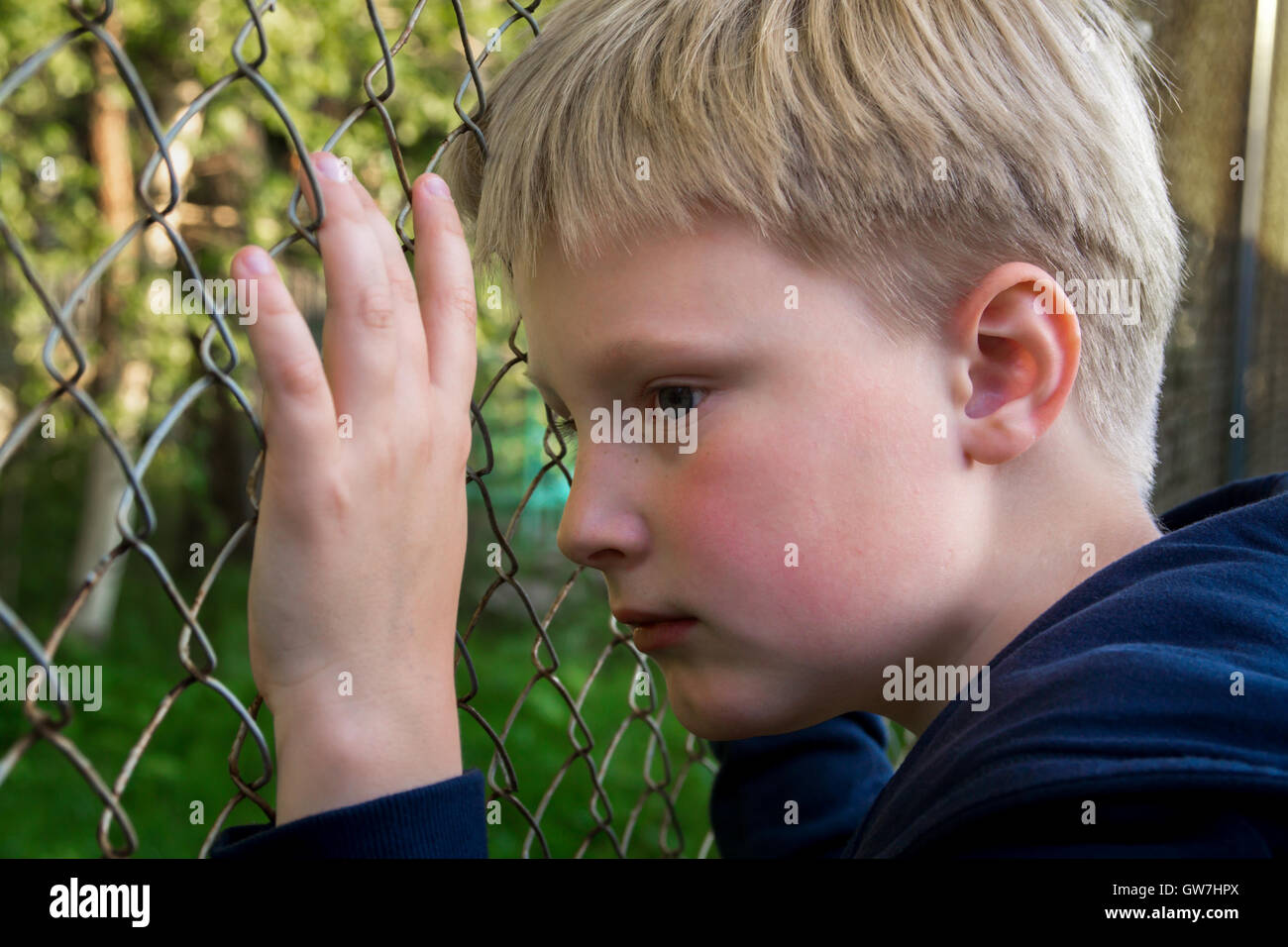 Triste, arrabbiato, frustrato boy (bambino, capretto, teen) vicino a maglia metallica, close up ritratto, bambini concetto problemi Foto Stock