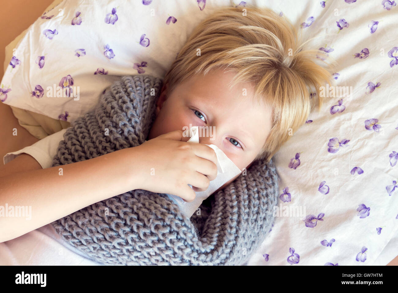 Ammalati bambino ragazzo soffia il naso che stabilisce nel letto con la faccia triste - Salute e medicina concept Foto Stock