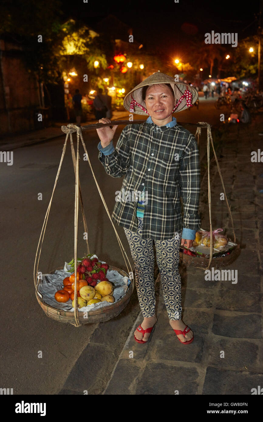 Donna vietnamita che trasportano produrre su un giogo di bambù, Hoi An (Patrimonio Mondiale dell'UNESCO), Vietnam Foto Stock