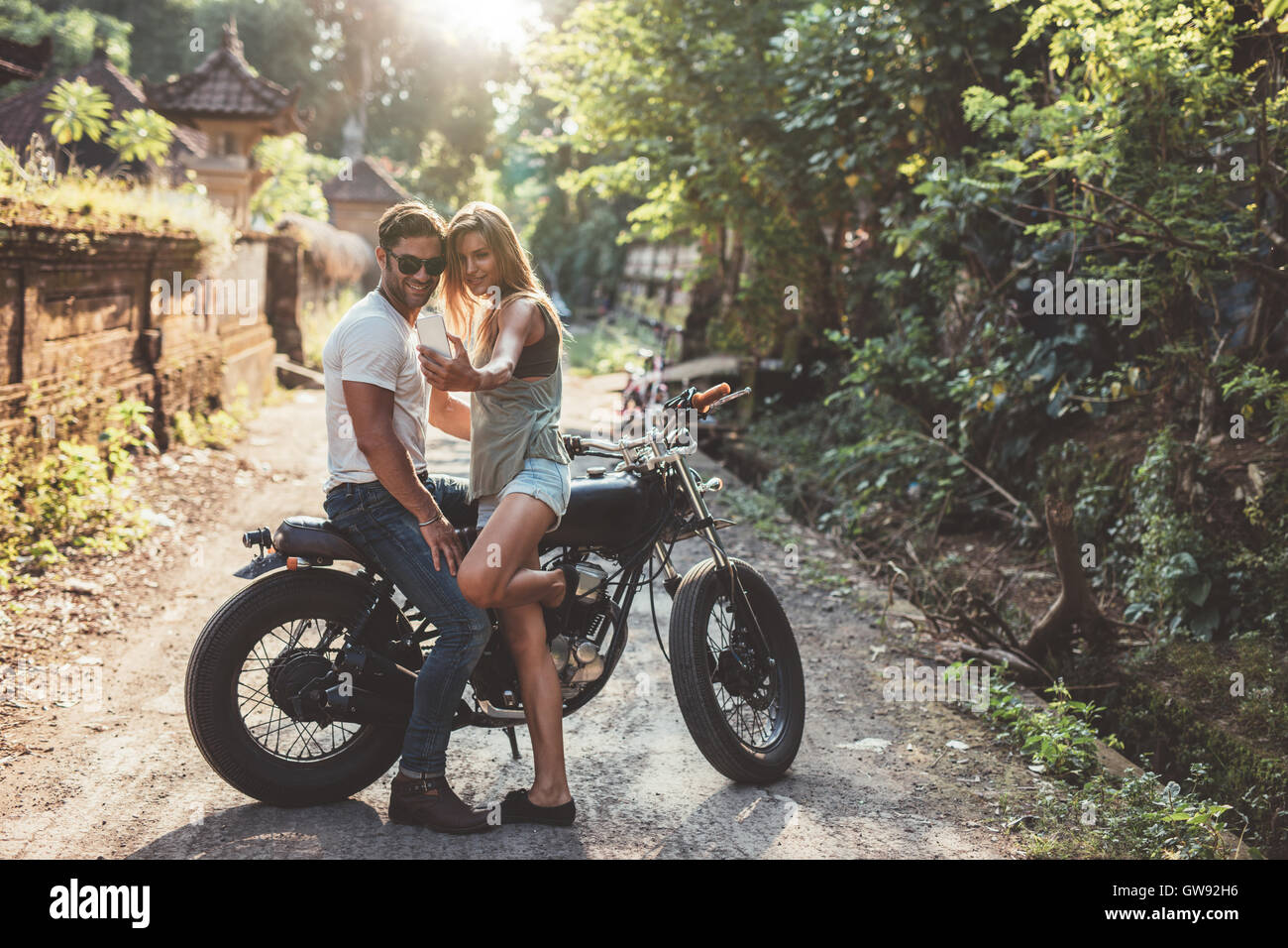 Colpo di amorevole coppia giovane prendendo un selfie con la motocicletta sulla strada del villaggio. Giovane donna e uomo prendendo auto immagini con mobil Foto Stock