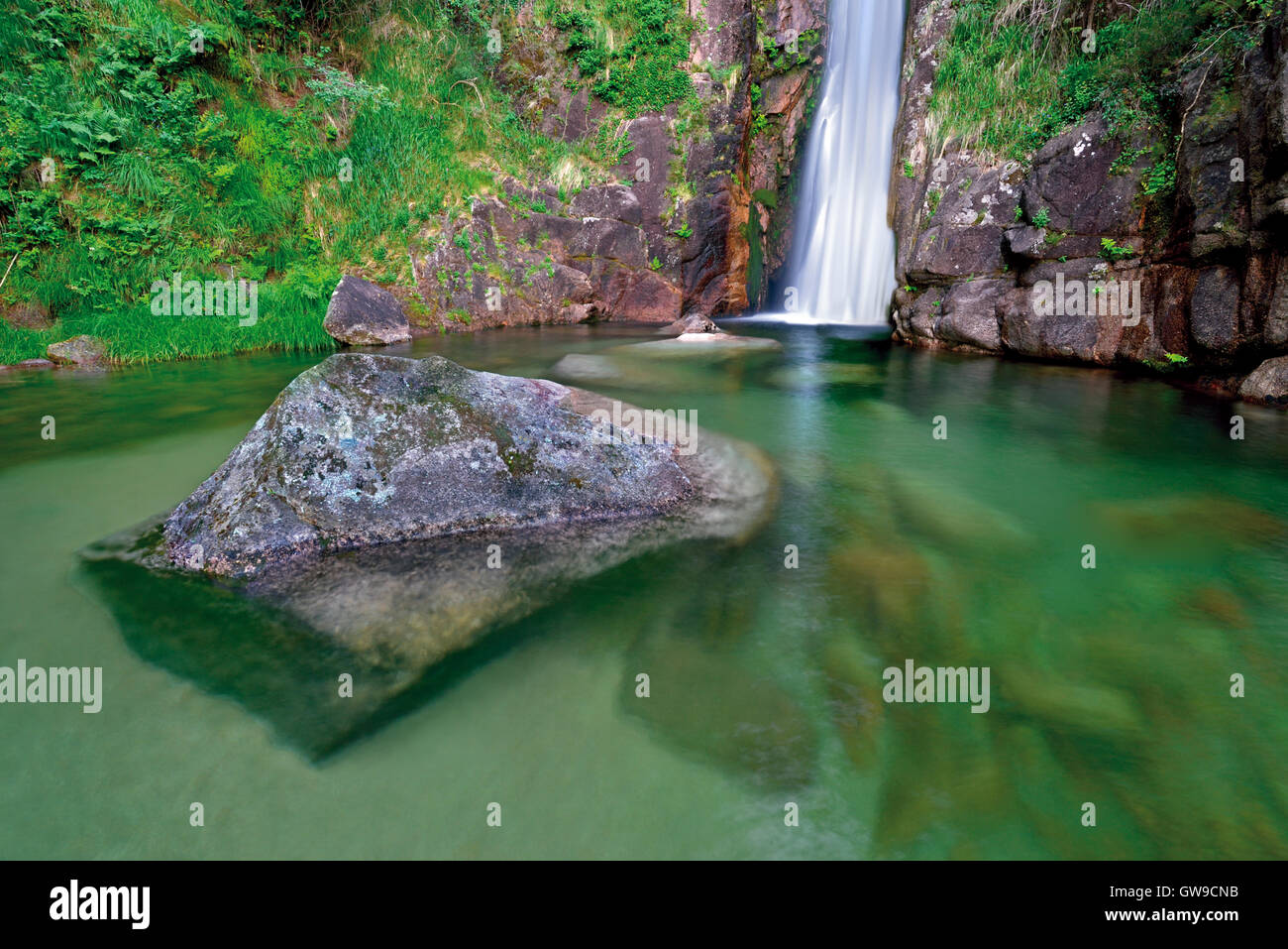 Portogallo: Cascata con piscina naturale e enorme roccia in acqua trasparente Foto Stock