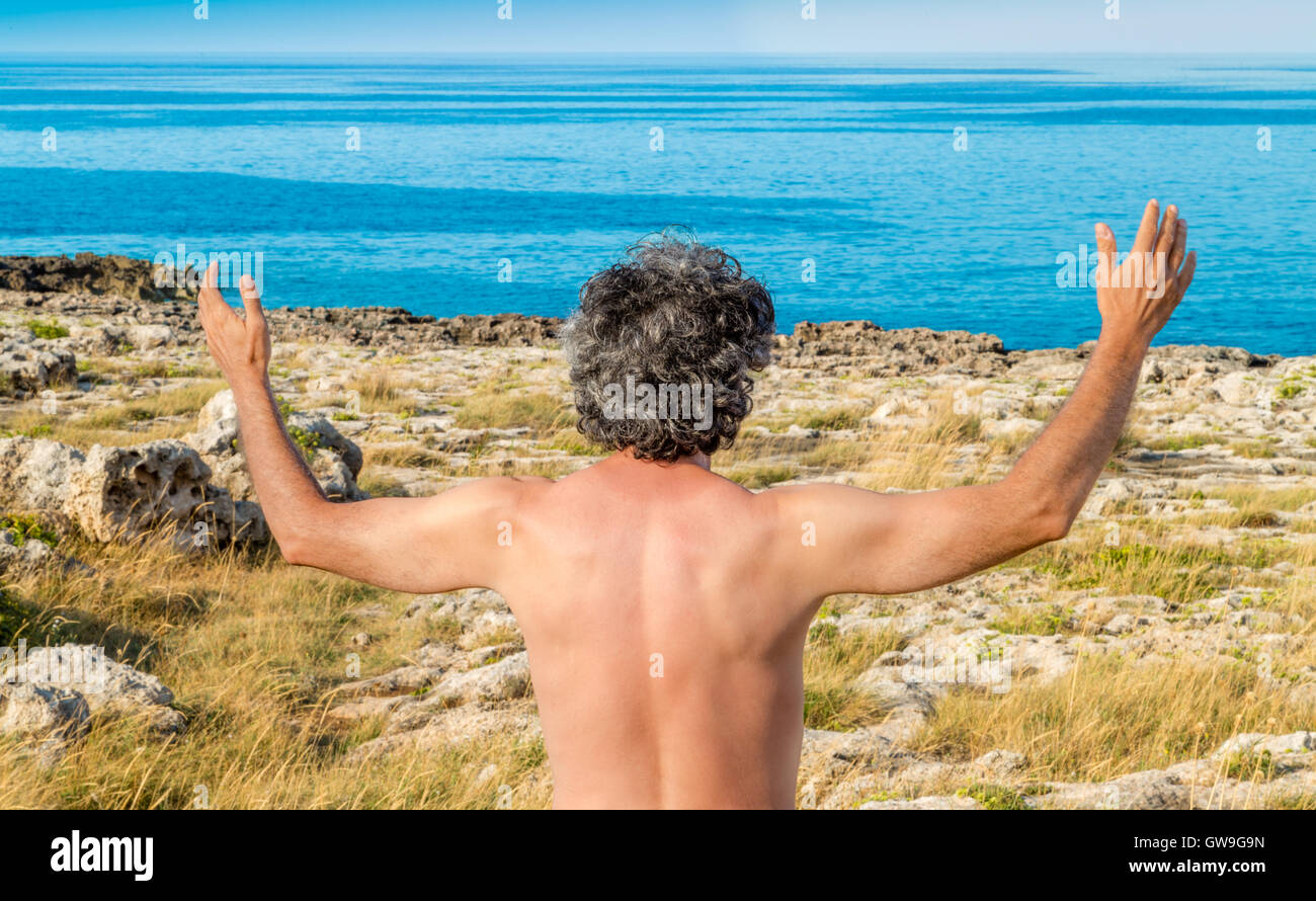Uomo maturo alzando le mani per mare Foto Stock