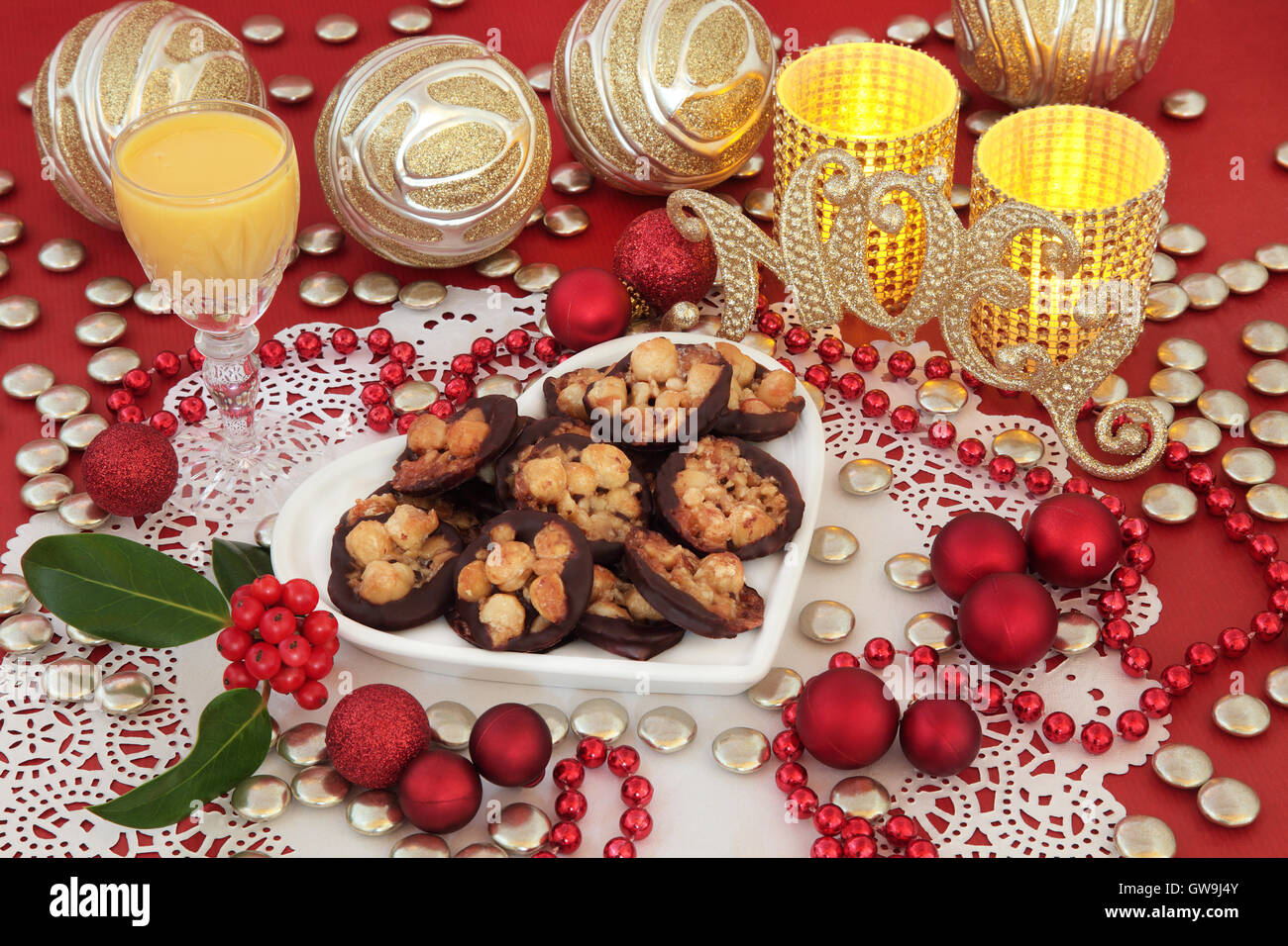 Natale ancora in vita con biscotti fiorentina, oro glitter noel segno, zabaione, agrifoglio, candele e decorazioni su un rosso. Foto Stock