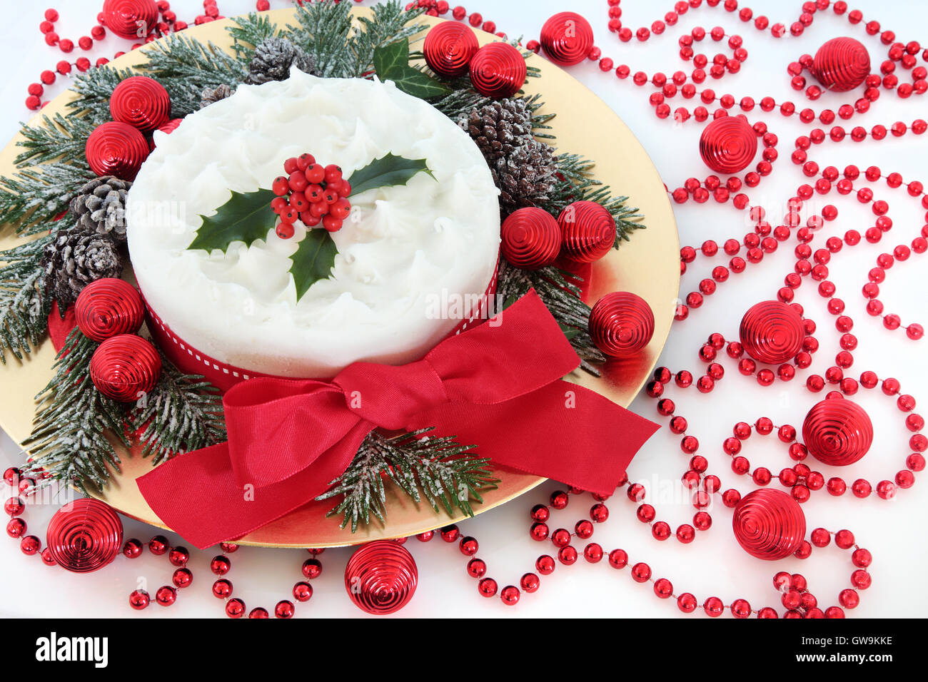 Torta di Natale con glassa e holly bacche, coperta di neve in inverno verde, rosso baubles, perline e nastri con la prua. Foto Stock