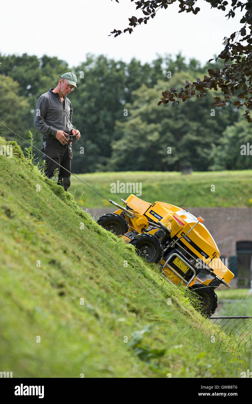 Un controllo remoto industriale taglierina di erba su una pendenza ripida parete della città della città di Naarden vesting. Foto Stock