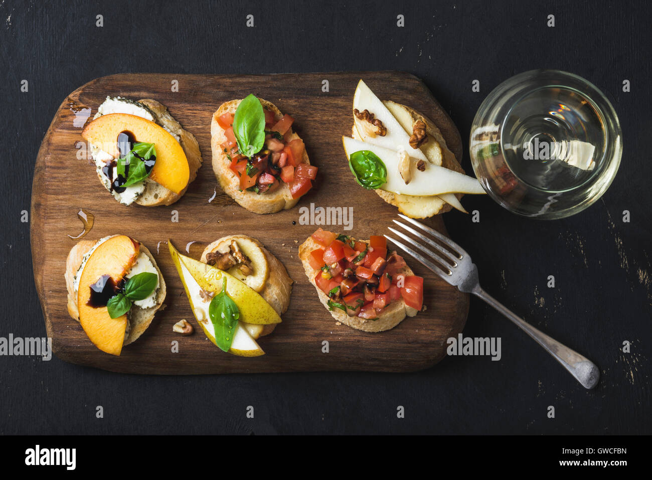 La bruschetta insieme con un bicchiere di vino bianco. Nero lo sfondo di legno compensato, vista dall'alto, composizione orizzontale Foto Stock