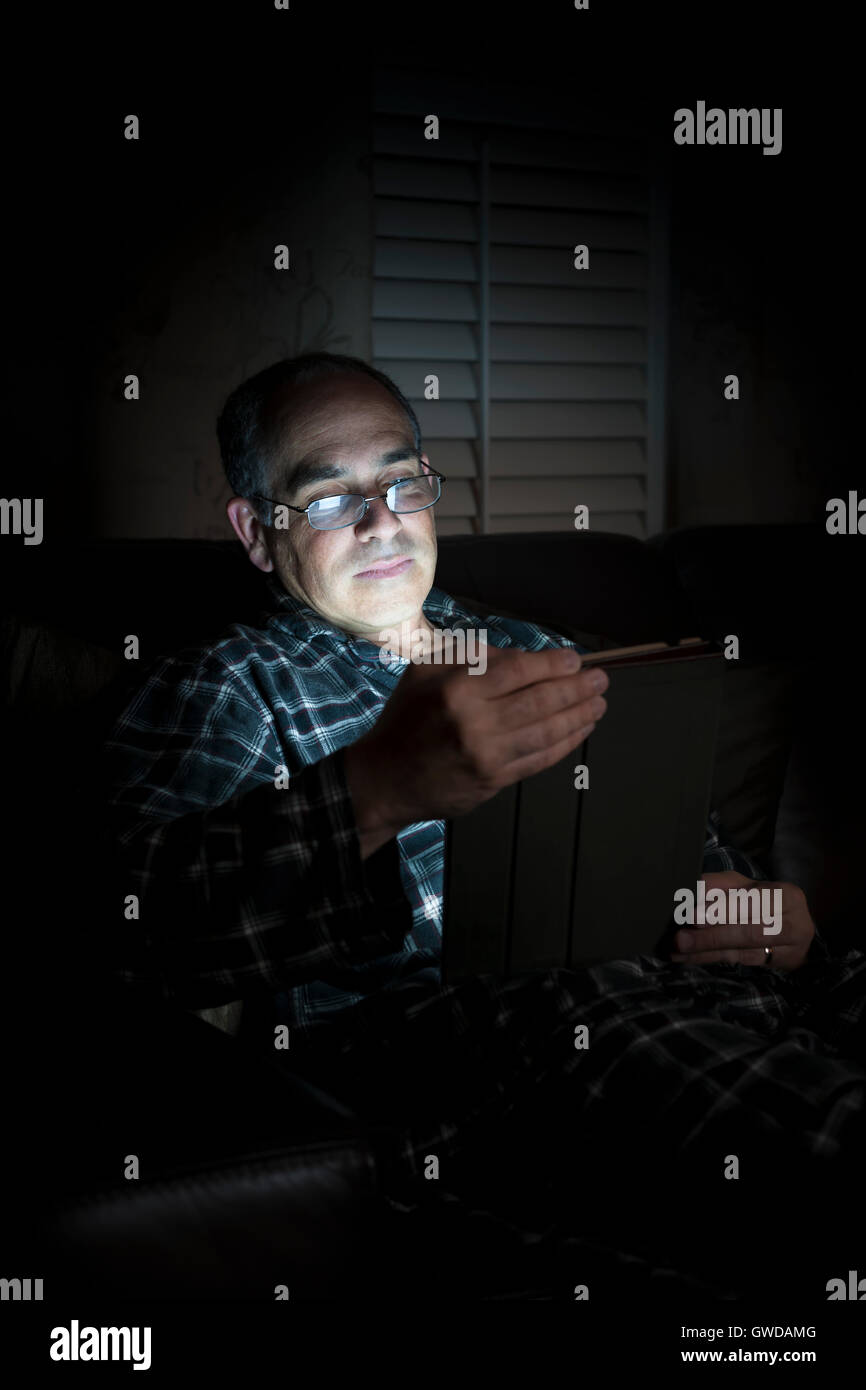 Uomo di mezza età in pigiama tablet di lettura di notte Foto Stock