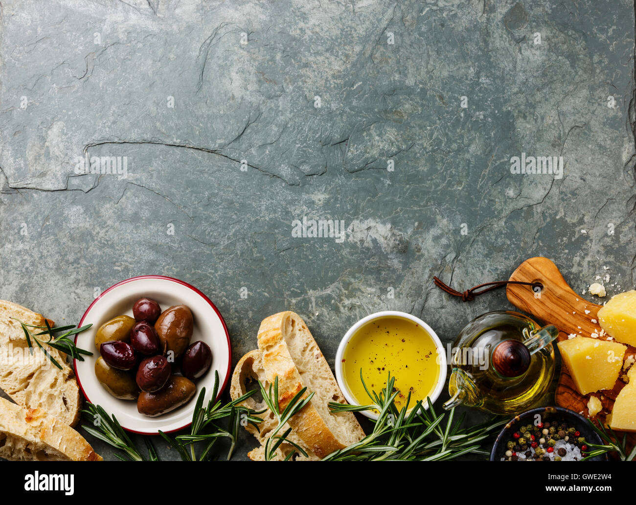 Il cibo italiano ingredienti sfondo con fette di pane Ciabatta, parmigiano, olio d'oliva, le olive e il rosmarino sulla pietra grigio ardesia Foto Stock