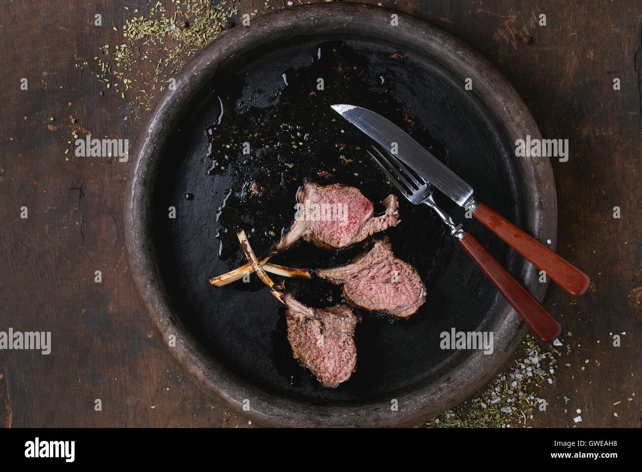 Tritate il barbecue grigliate carré di agnello, servita con il condimento, forchetta e coltello sul vassoio di argilla su un vecchio sfondo di legno. Vista dall'alto. Foto Stock