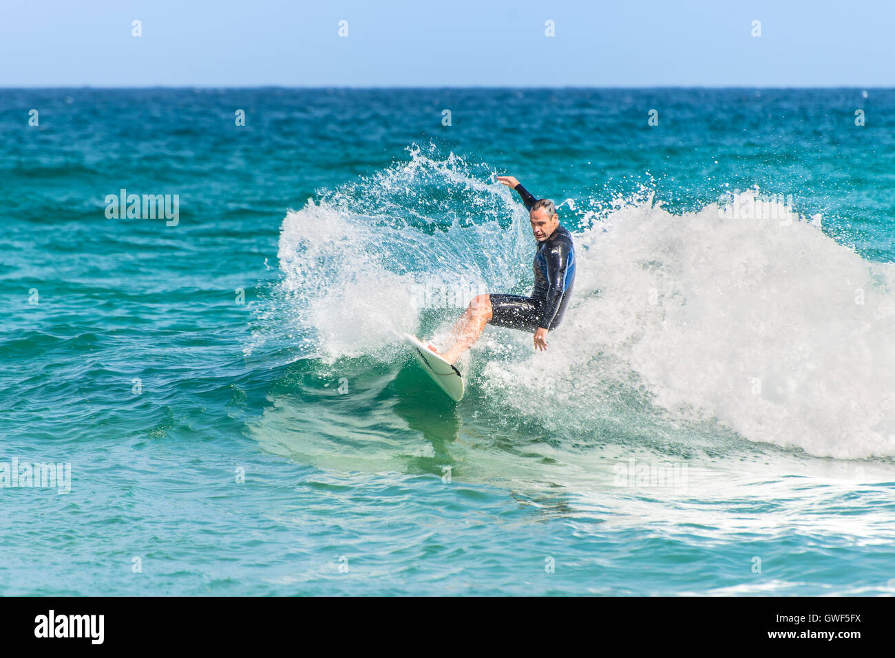 Un uomo che cavalca il suo surfboard verso la riva. Foto Stock