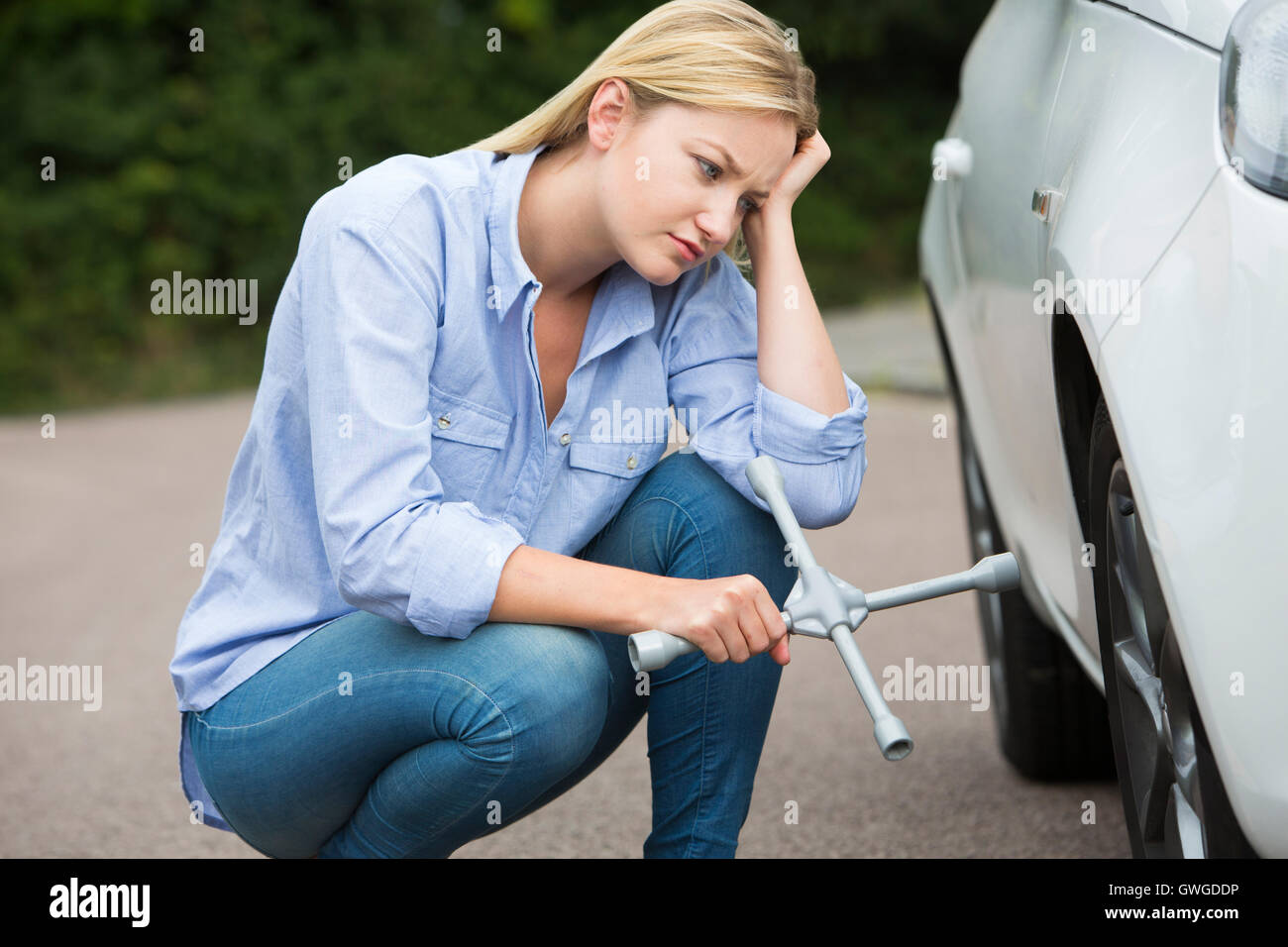 Frustrati Driver femmina con ferro di pneumatico cercando di cambiare la ruota Foto Stock