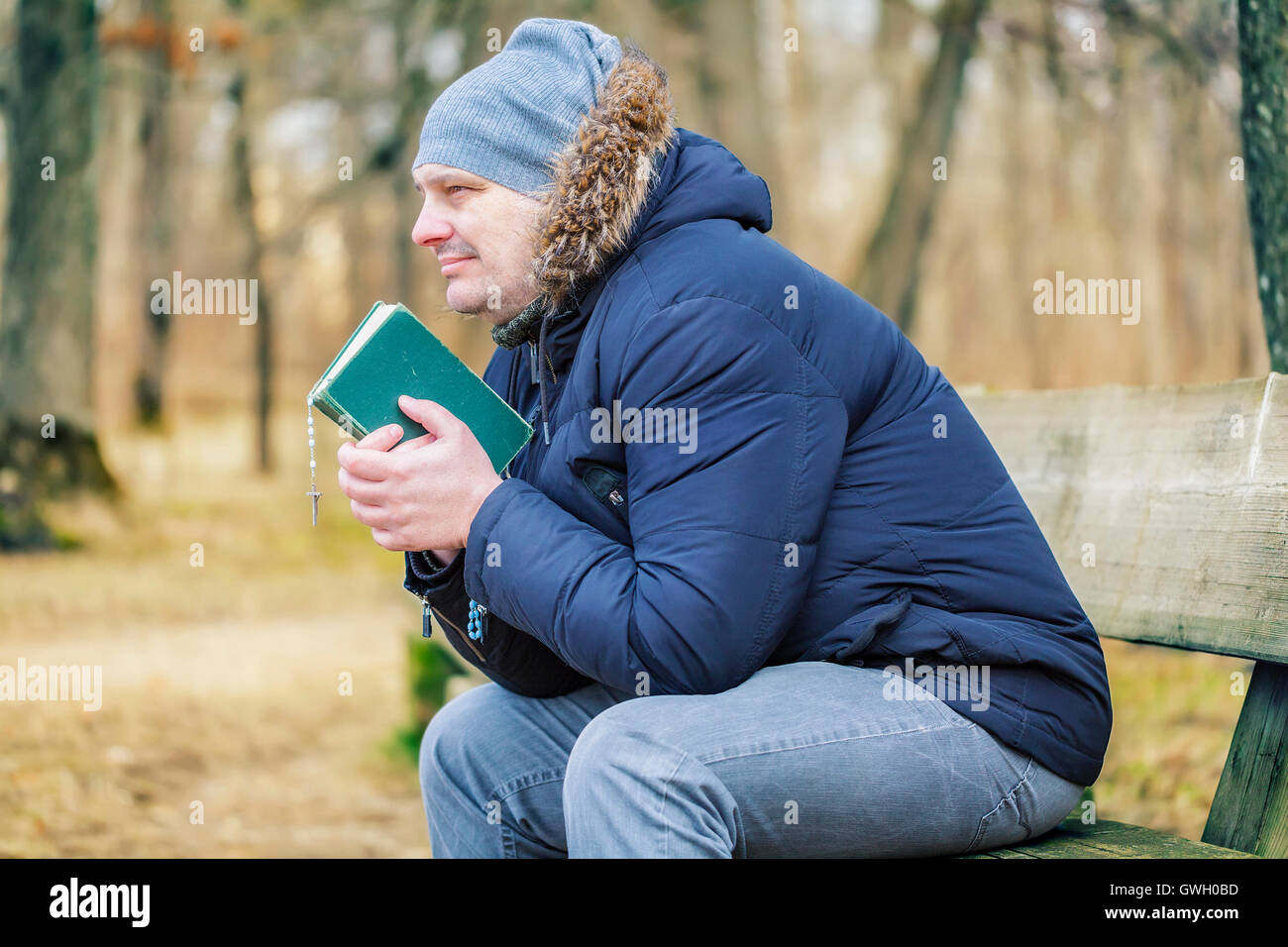 Uomo con la Bibbia e il rosario sul banco di lavoro nel parco Foto Stock