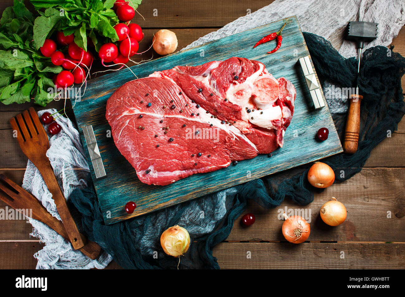 Carni fresche bovine Carne di vitello su tavola in legno rustico con utensili da cucina e verdure, vista dall'alto Foto Stock