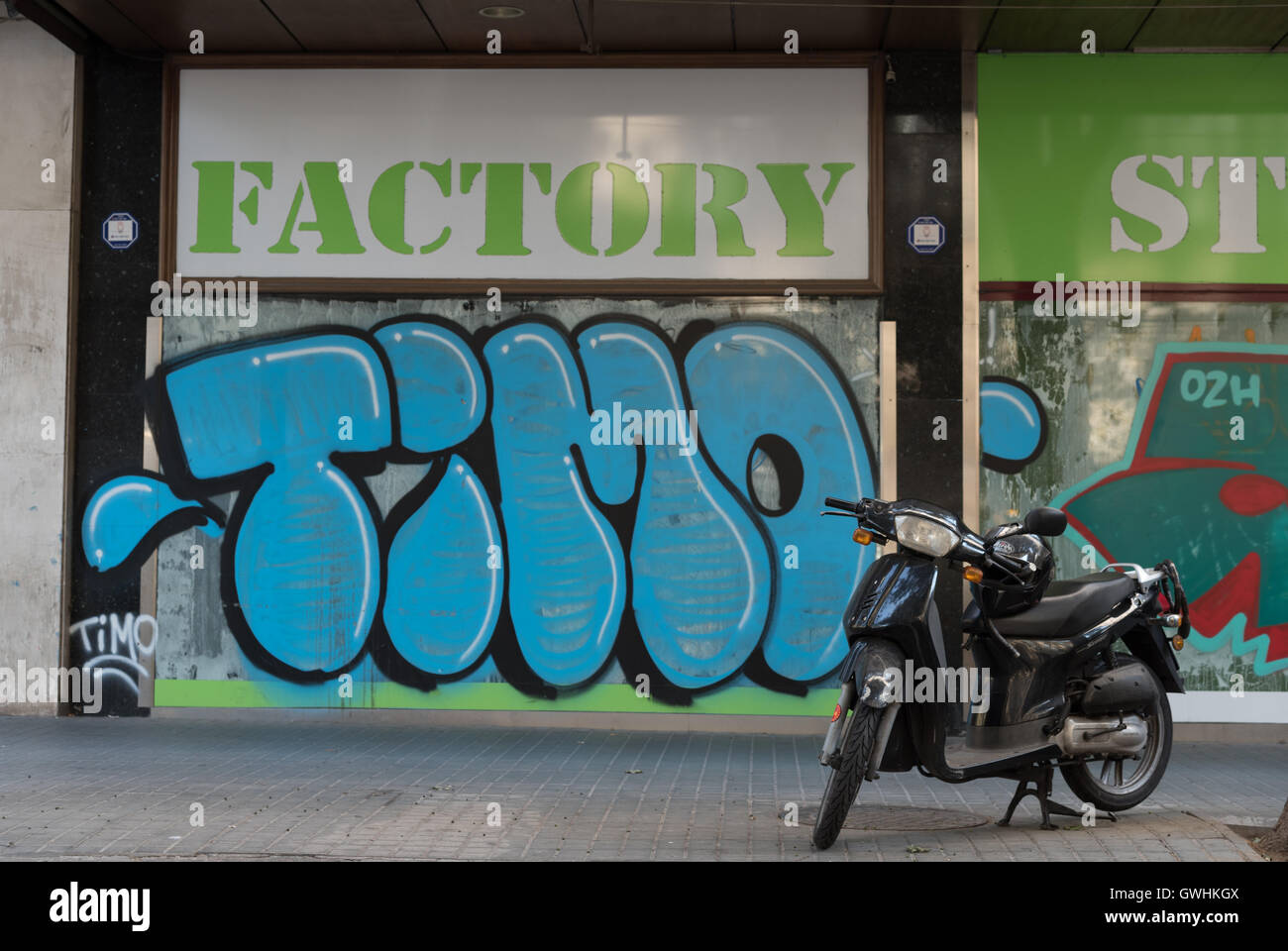 Coperto di graffiti shop anteriore e la moto a Barcellona. Il nome del negozio e fabbrica un tag lettura Timo dominano la scena. Foto Stock