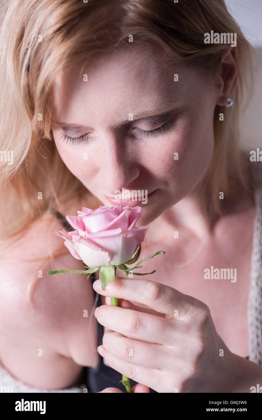 Bella donna bionda è annusare a una rosa in mano Foto Stock