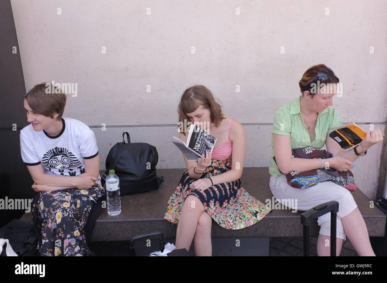 Persone con lettura a una stazione degli autobus Foto Stock