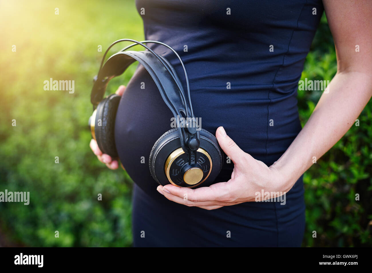 Donna incinta partecipazione delle cuffie sul suo stomaco Foto Stock