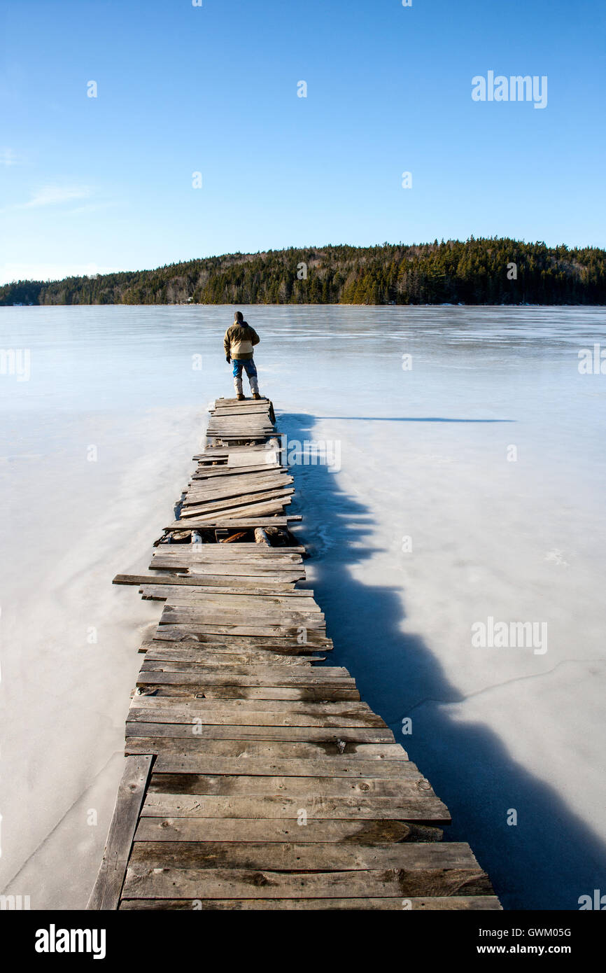 L uomo sta alla fine di un vecchio dock su un lago ghiacciato Foto Stock