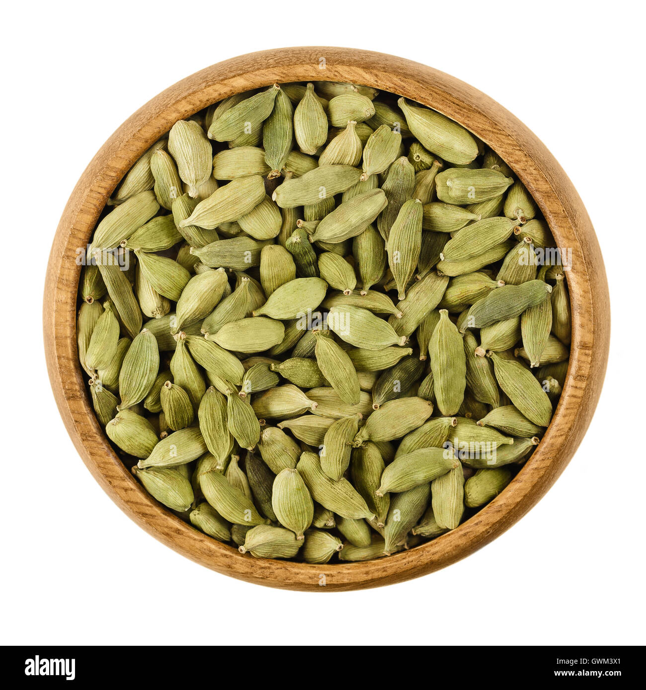 I semi di cardamomo in una ciotola di legno su sfondo bianco. Luce verde elaborato baccelli di Elettaria cardamomum, essiccato semi. Foto Stock