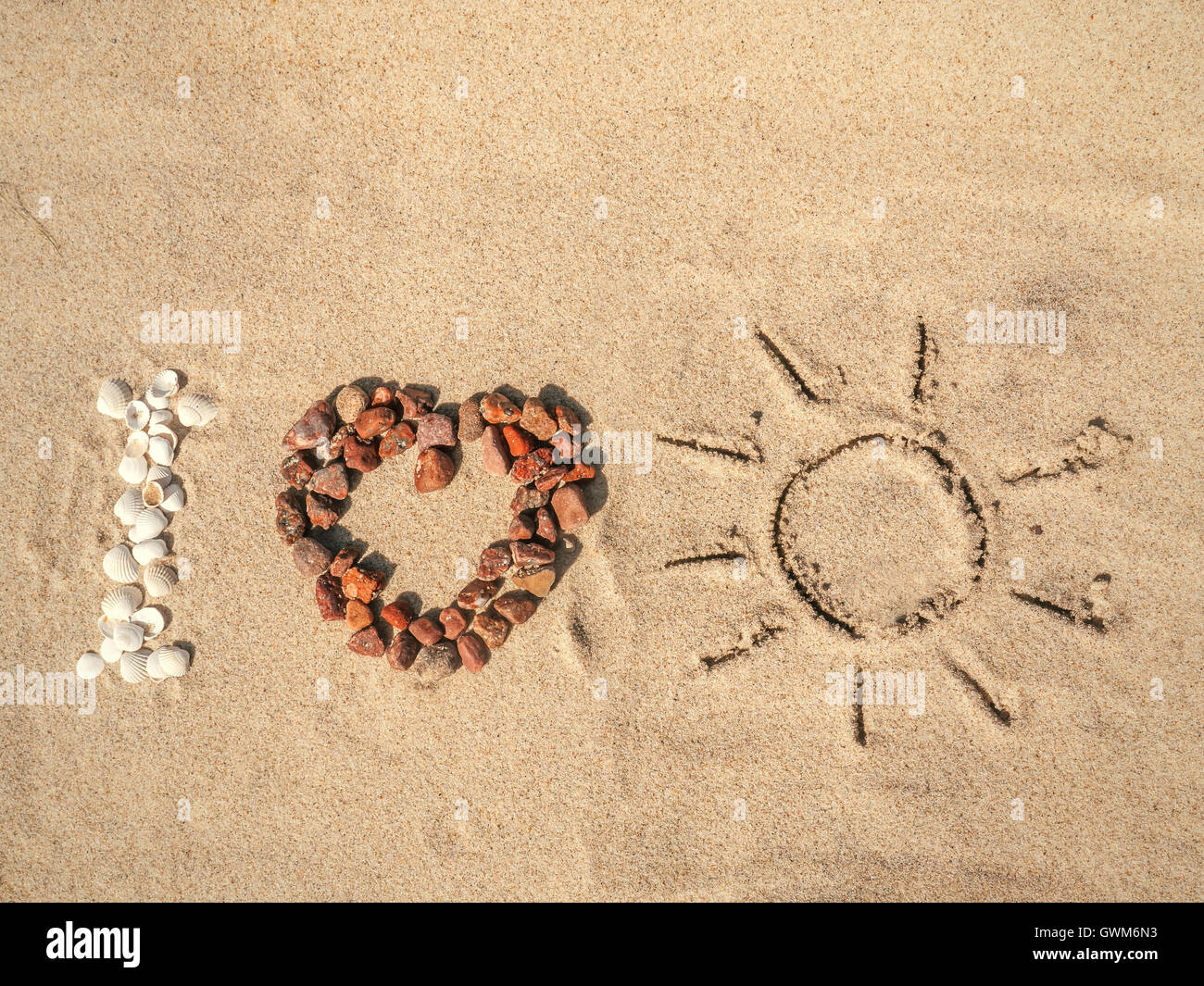Inquadratura concettuale di I Love Sun come acronimo disposti da conchiglie, rosso ciottoli e disegnati a mano segno di sole sulla spiaggia di sabbia Foto Stock
