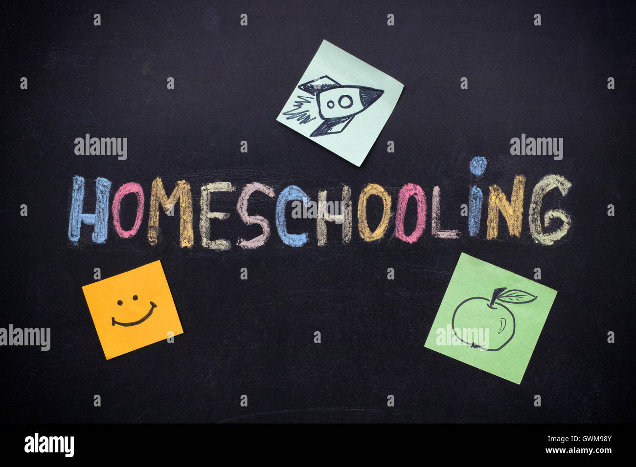 Homeschooling. Parola Homeschooling scrivere sulla lavagna con note su carta con un razzo su di esso, apple e sorriso. Close up. Foto Stock