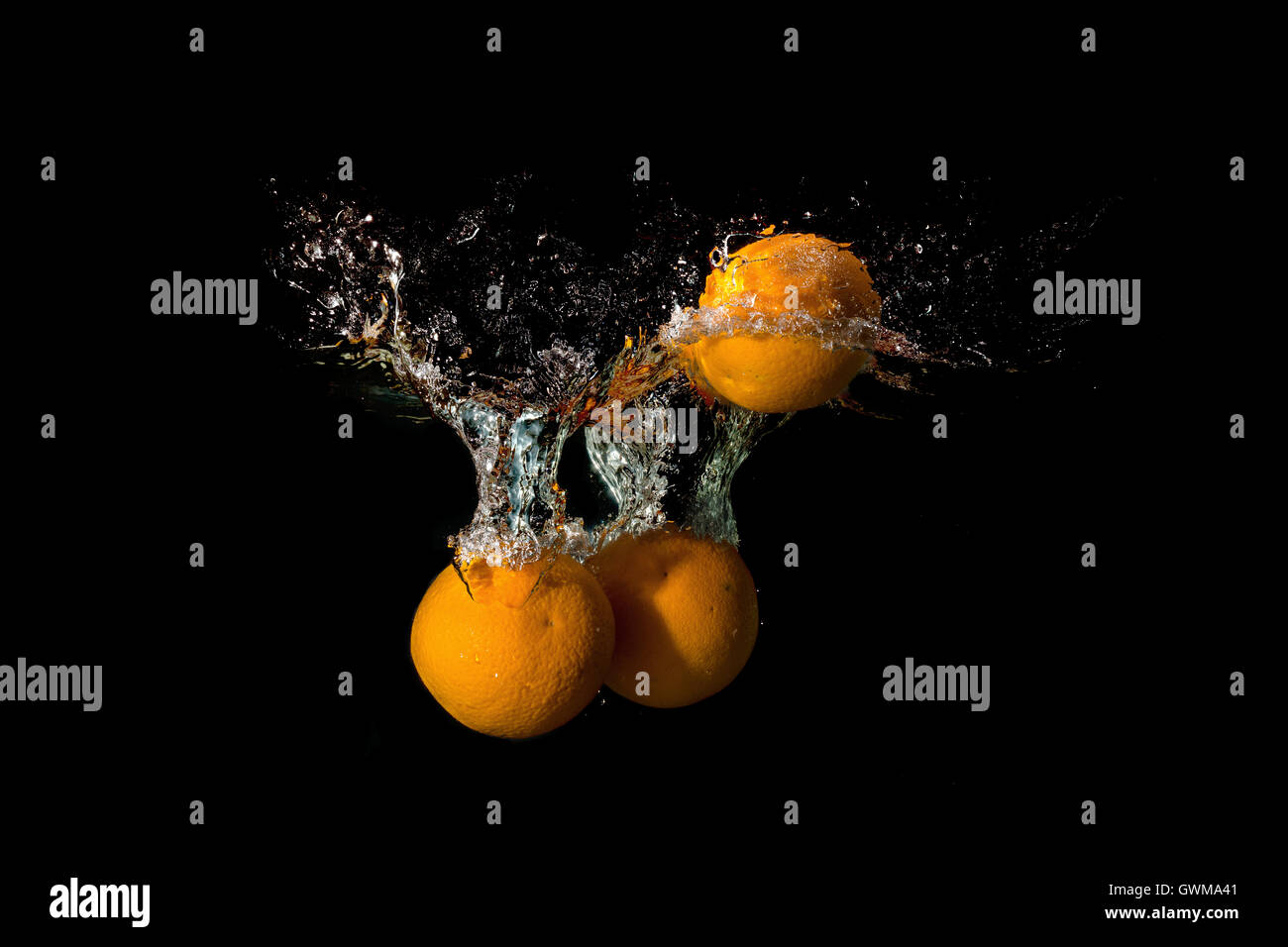 Tre arance in acqua sollevata una grande onda su sfondo scuro Foto Stock