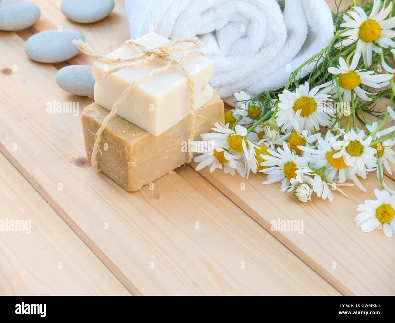 Laminato bianco asciugamano, saponette legati con corda di iuta e mazzo di fiori di camomilla in legno naturale sfondo tavole Foto Stock