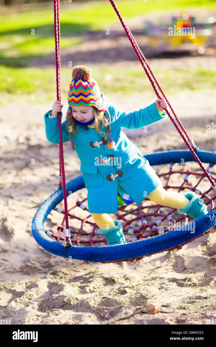 Bambina in caldo cappotto e hat su un parco giochi. Bambino che gioca all'aperto in autunno. Bambini giocano sul cortile della scuola Foto Stock