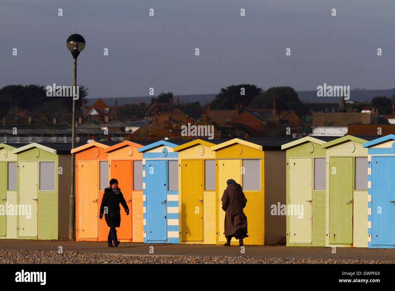 La gente a camminare lungo la linea di cabine in legno sul fronte mare su un pomeriggio invernale, Seaford, East Sussex, Inghilterra Foto Stock