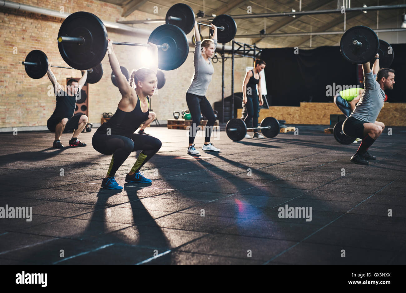 Un gruppo di giovani adulti muscolare maschi e femmine sollevamento grandi barbells in cross-fit classe con tappetini spessi e muri di mattoni Foto Stock