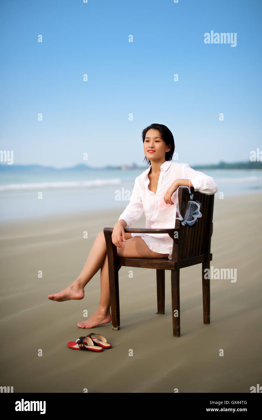 Ragazza seduta su una sedia presso la spiaggia di fare vacanza Foto Stock
