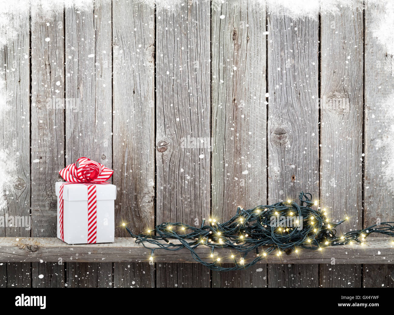 Le luci di Natale e confezione regalo nella parte anteriore della parete di legno con la neve. Vista con copia spazio per il testo Foto Stock