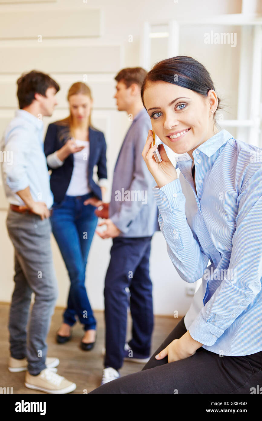 Giovane donna comunicazione con il suo telefono cellulare nel corso di una riunione del team Foto Stock