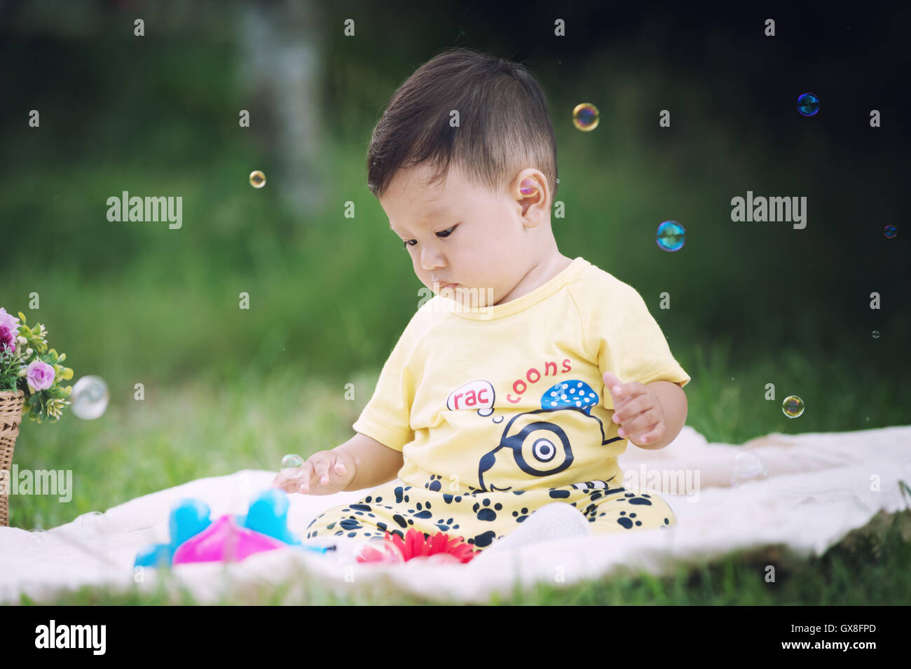 Asia bambino seduto sul prato verde nel parco con bolle di sapone Foto Stock